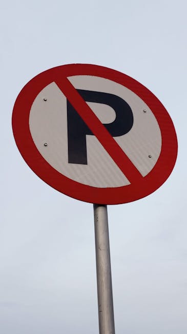 A circular no parking sign with a blue background and a red border, mounted on a metal bracket attached to a red-brick wall. The wall consists of evenly laid bricks in shades of red, brown, and tan, w